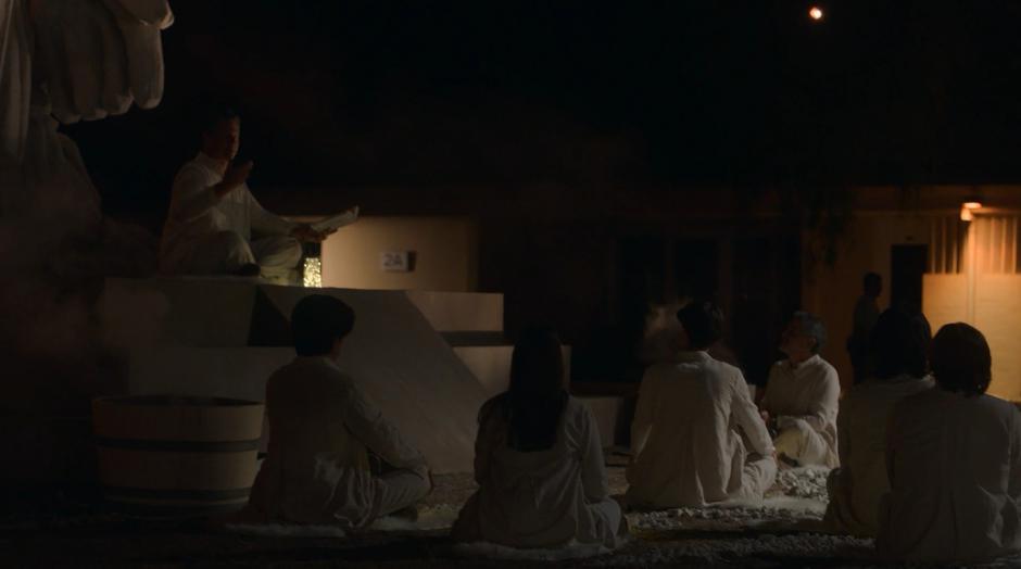 Frank sits beneath the statue and preaches to a group of disciples.