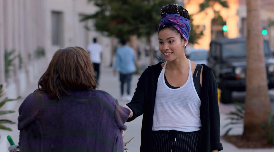 A woman hands Xavin a energy bar while Xavin is disguised as a homeless woman.