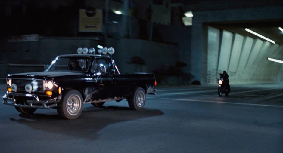 The Terminator holds his gun towards the truck driven by Sarah Connor while they both drive out of the tunnel.