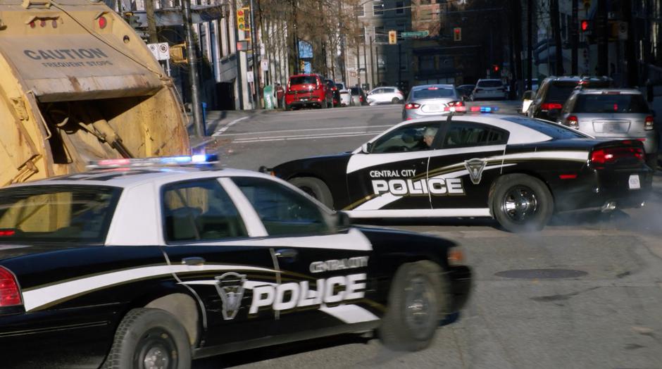 Two squad cars swerve to a stop after being stopped by a garbage truck.