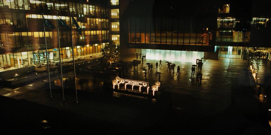 People mill around in front of the building at night.