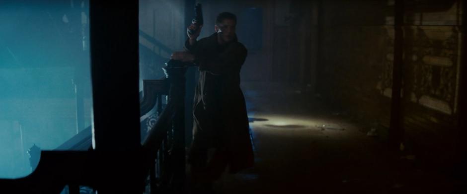 Deckard holds up his gun as he gets to the top of the stairs and heads towards the apartment.