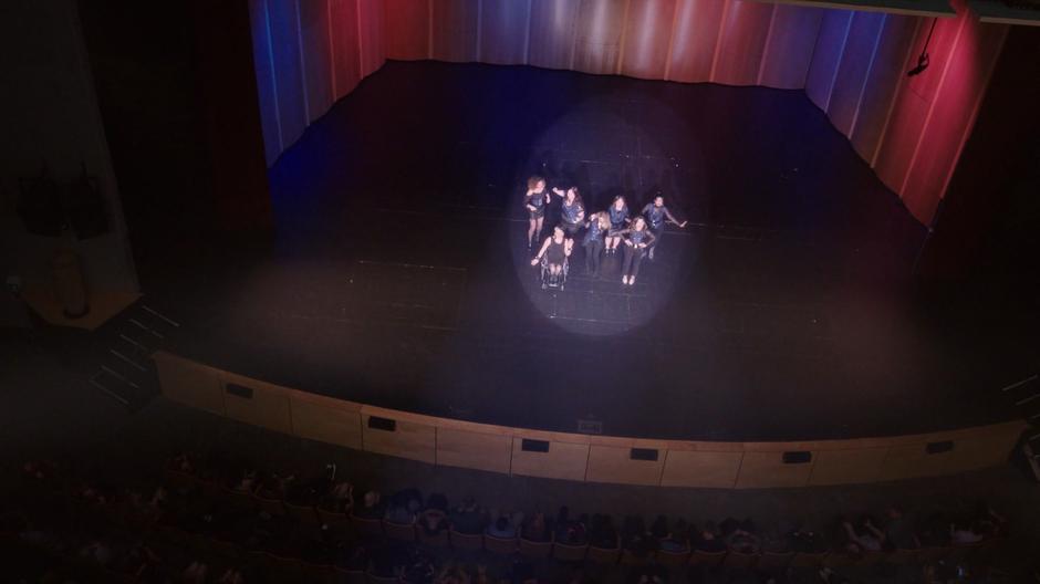 The music group are visible below lit by the spotlights as the audience watches with rapt attention.