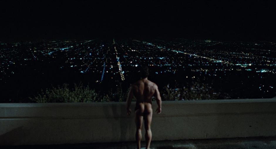 A very naked Terminator stands on the edge of the plaza and looks out over the city.