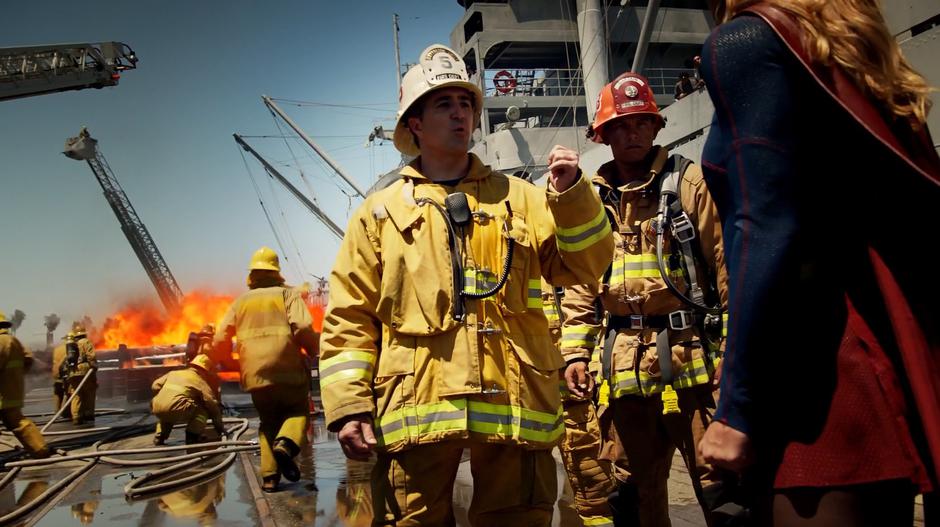 A firefighter tells Supergirl about the fire behind him.