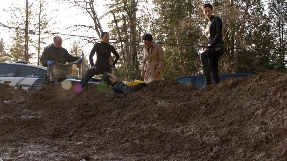 Colonel Haley and Alex stand on the edge of the crater over Chuck Grossman's body while a DEO agent talks about his injuries.