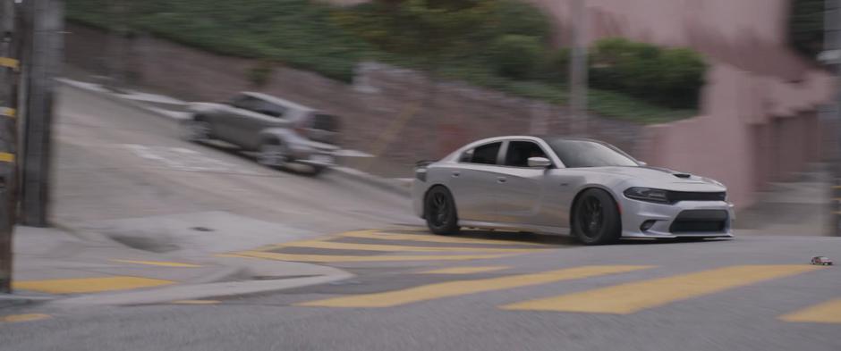 A pursuing car tries to follow Luis's shrunken car around the corner.