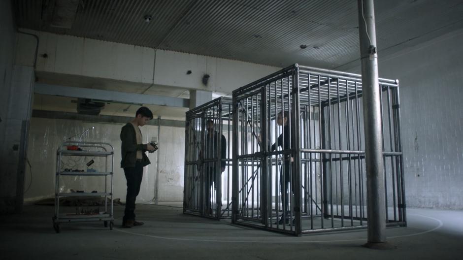 Daniel Stoppard messes with his device while Penny and Marina watch him from the cages.