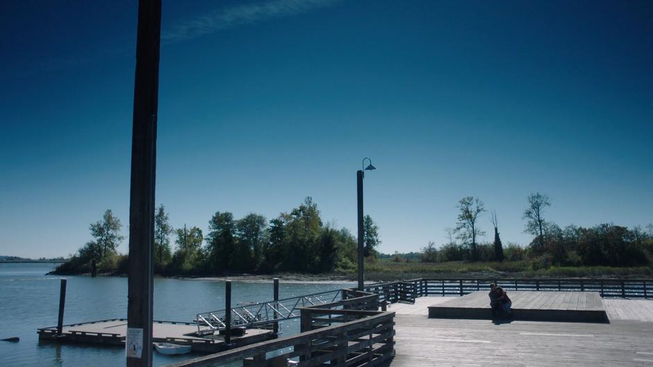 Ben holds Maddie while they sit down on a platform on the dock.