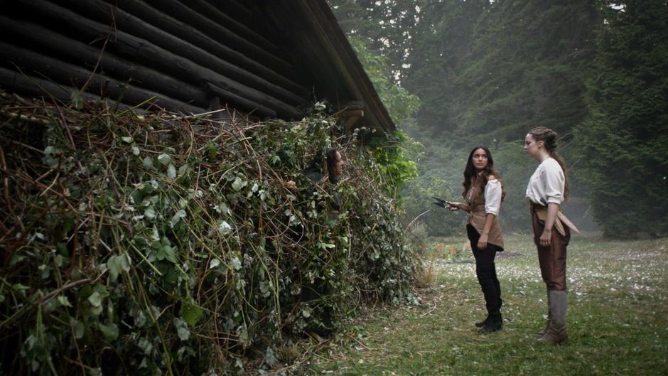 Margo holds the sheers out at the prophet who is stuck in the ivy while looking at Fen.