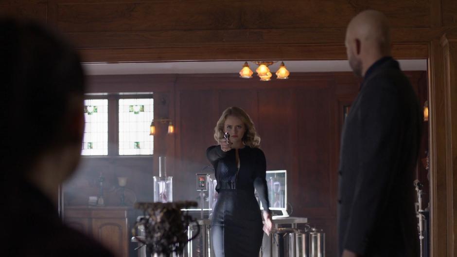 Lena and Lex look at Eve as she walks in with her gun held up while wearing a evil black outfit.