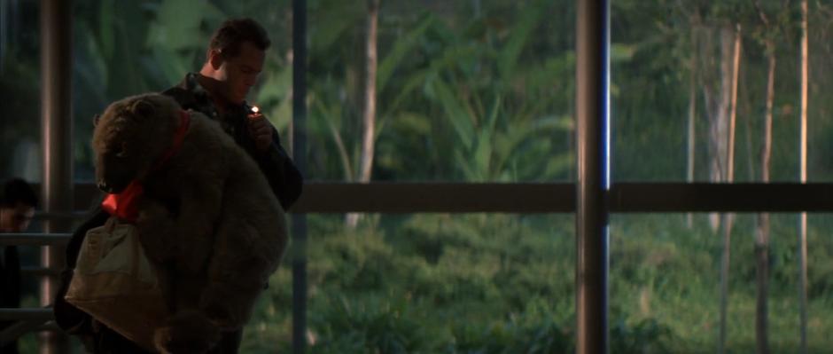 John McClane lights his cigarette in the baggage claim while holding a giant stuffed bear.