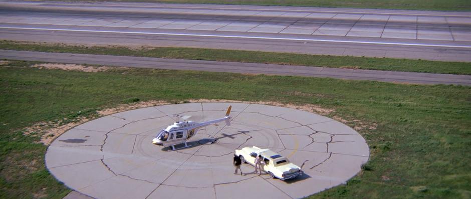 Bond exits the car and walks over towards the waiting helicopter.