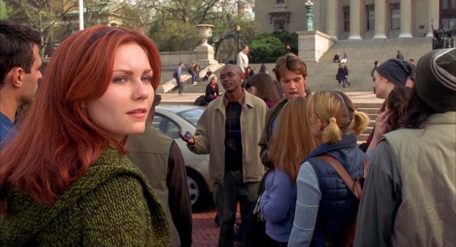 Mary Jane looks over her shoulder while the teacher talks to her class out front of the building.