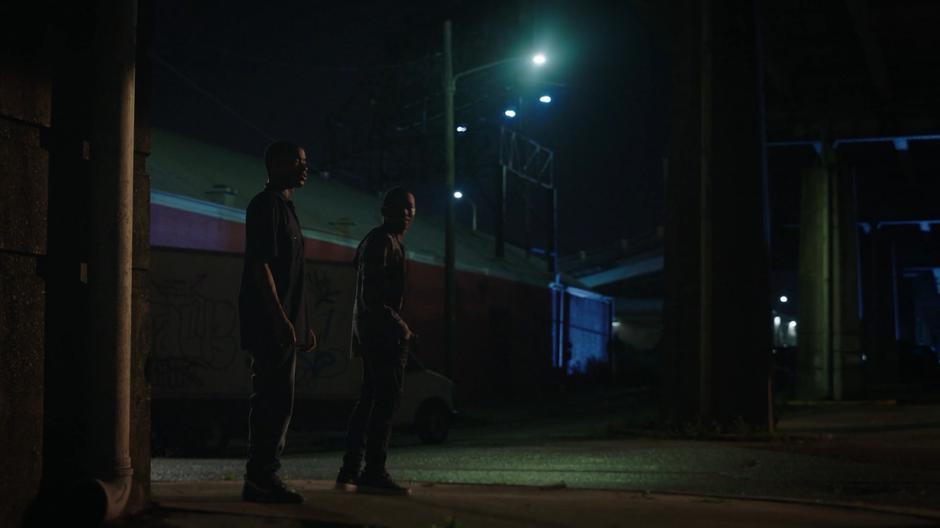 The two gang members look around while waiting on the street corner.