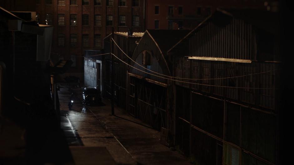 The gang courier drives down the alley towards the warehouse on his motorcycle.