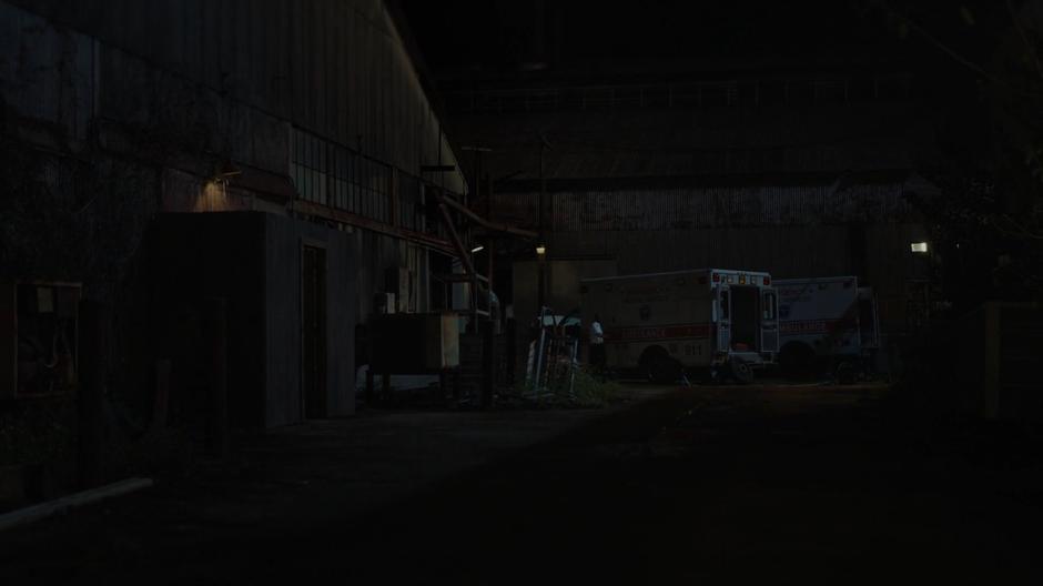 An ambulance driver walks around his ambulance in the distance.