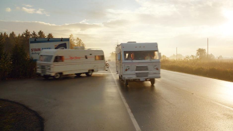 The RV turns off the highway behind the billboard while its duplicate continues down the road.