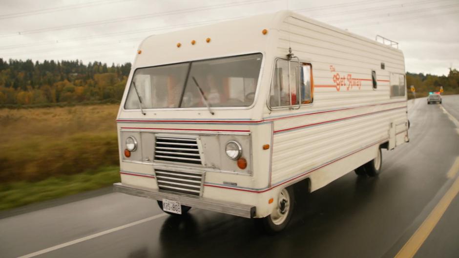 The RV is chased down the highway by the police car driven by Hank.