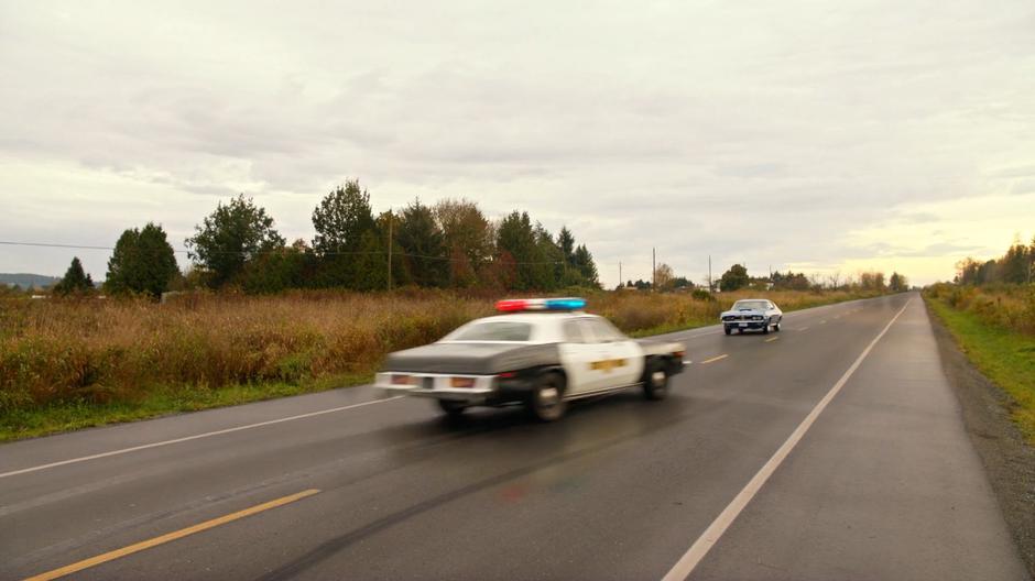 The police car races down the highway after taking a u-turn.