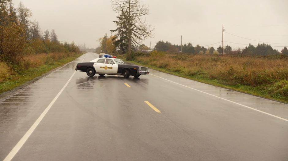 The police car turns around in the middle of the street and drives off in the other direction.