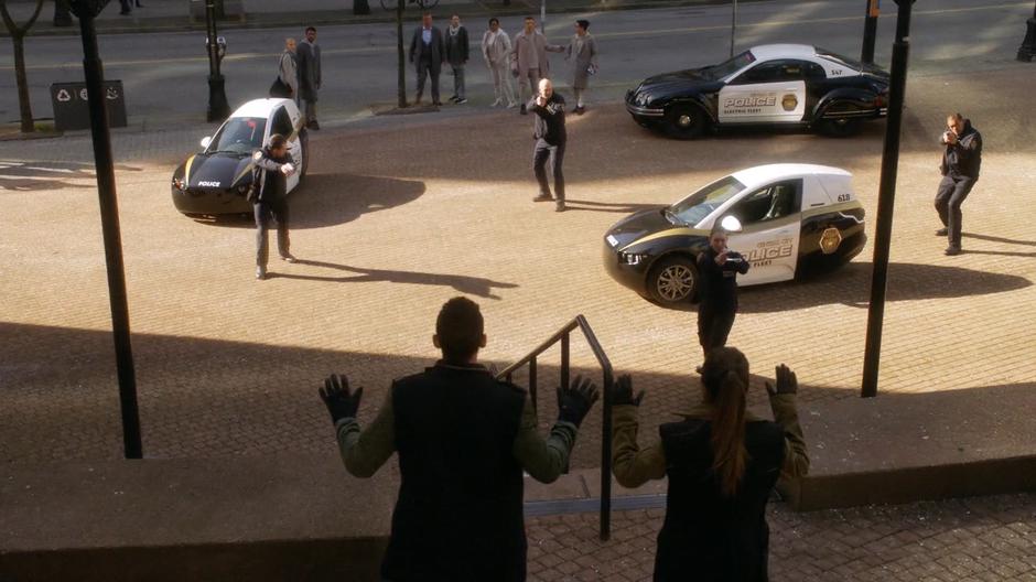 The two bank robbers hold up their hands as several police officer hold them at gunpoint.