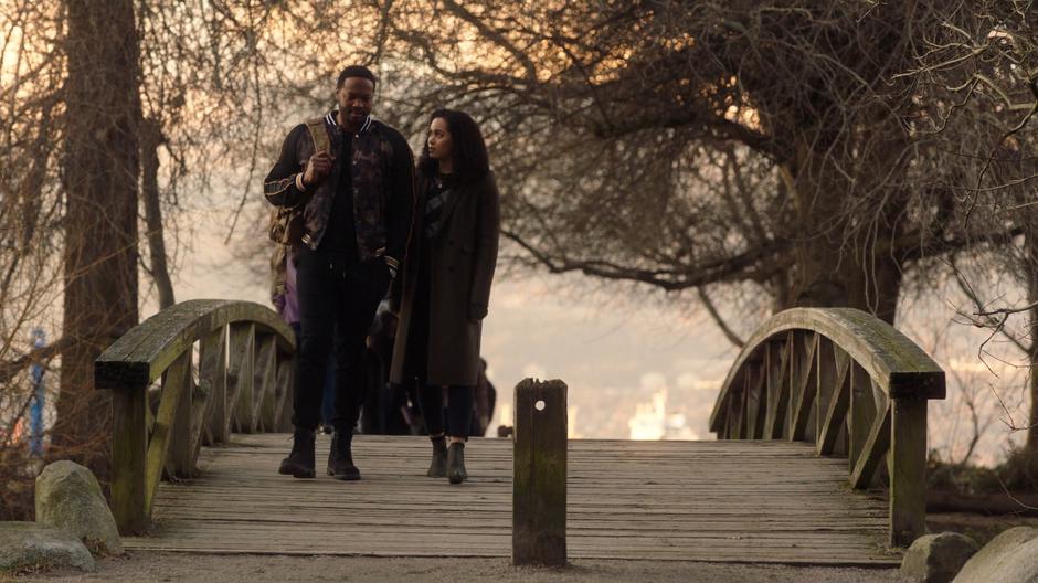 Macy looks over at Galvin as they walk across a wood bridge.