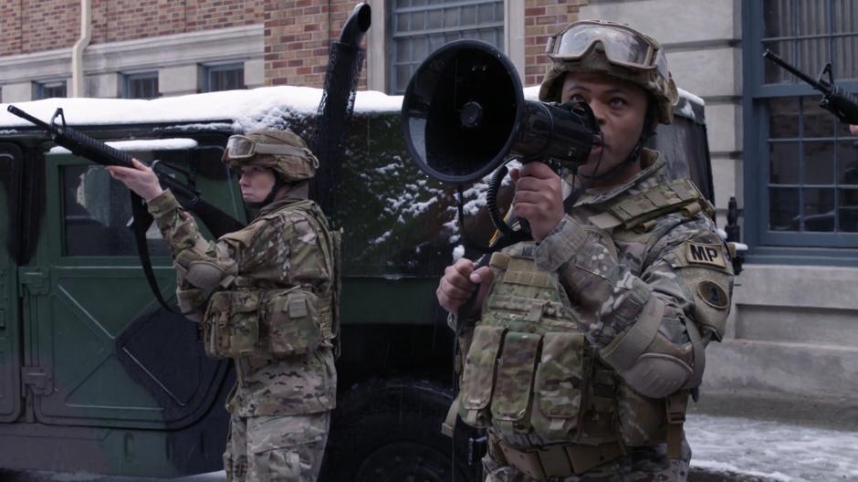 A soldier calls out to Supergirl through a bullhorn telling her to surrender.