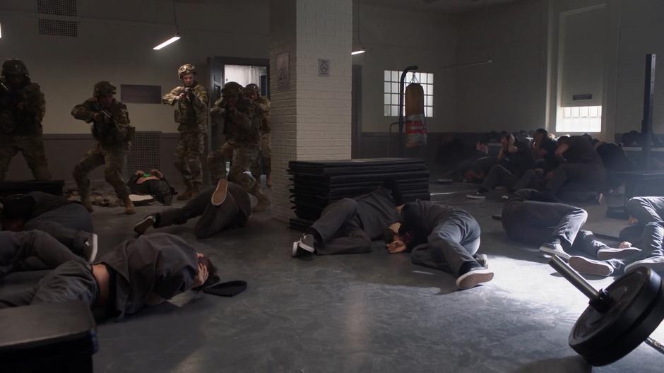 The soldiers storm into the weight room where all of the inmates are lying on the floor.