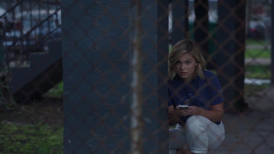 Tandy crouches beneath the porch of a house from across the street as she waits for Mikayla to leave.