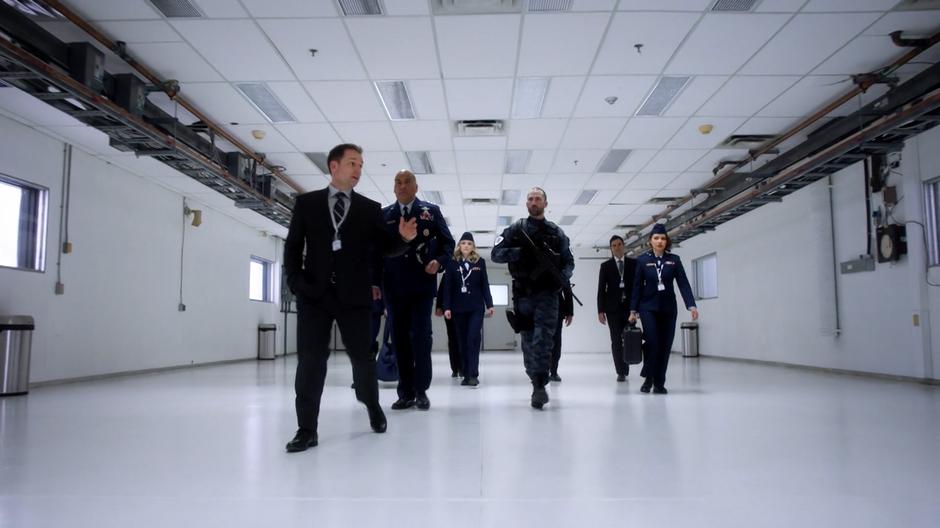 An employee of McCulloch Technologies leads Nora and the other Rogues on a tour of the building under heavy guard.