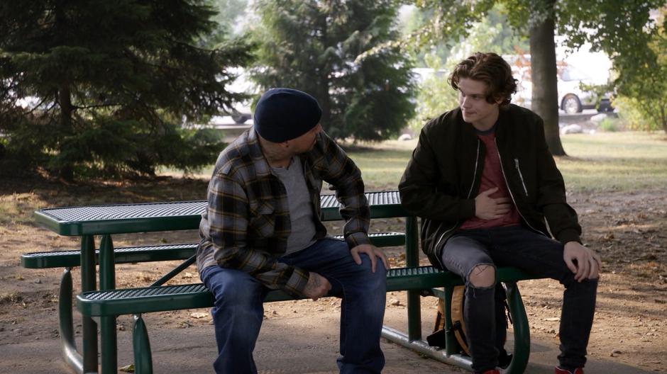 Oliver chats with Baron while they are sitting on a picnic table.