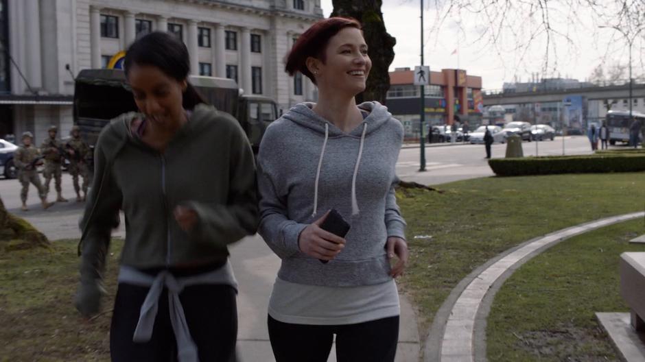 Kelly and Alex smile while jogging with one another past the military.