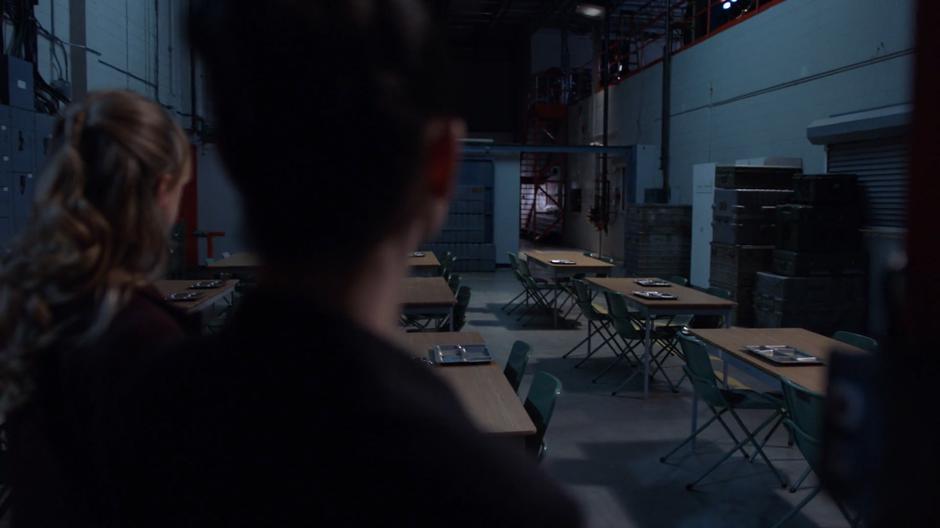 Kara and Lena look out over the lab's cafeteria after turning on the lights.