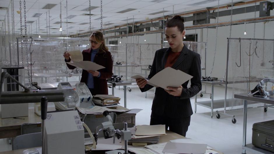 Kara and Lena look through the paper files on the aliens that were being experimented on by Lex and the Kasnians.