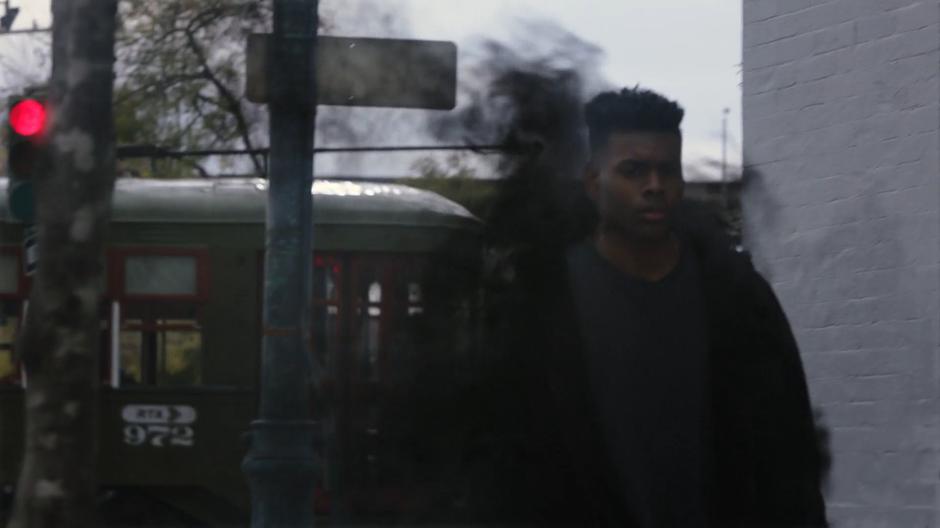 Tyrone appears on the street in a cloud of smoke as the streetcar continues driving past to the stop.