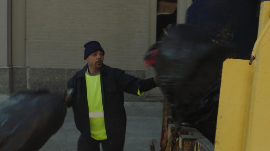 A garbage collector throws a bag of trash into the back of his truck.