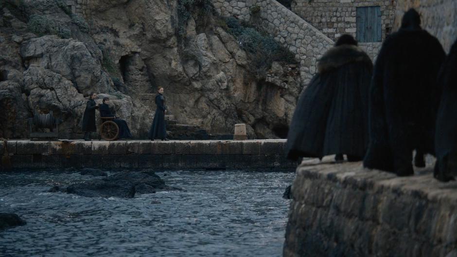 Arya, Bran, and Sansa wait on the small dock as Jon is escorted towards them.