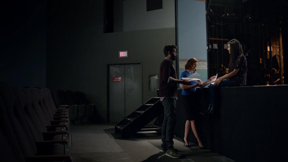 Ravi and Peyton read the new script in front of Yasmine who patient waits sitting on the edge of the stage.