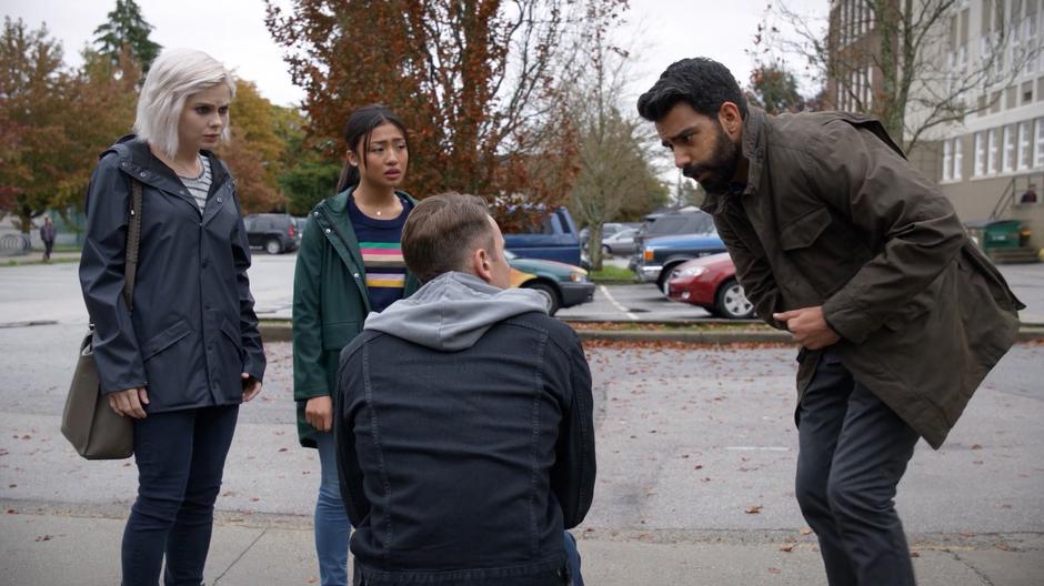 Liv and Amy watch as Ravi leans down to examine Jamie.