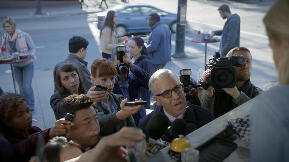 A reporter in the middle of a group of reporters asks Dolly Durkins how she knows about the brain supply problem.