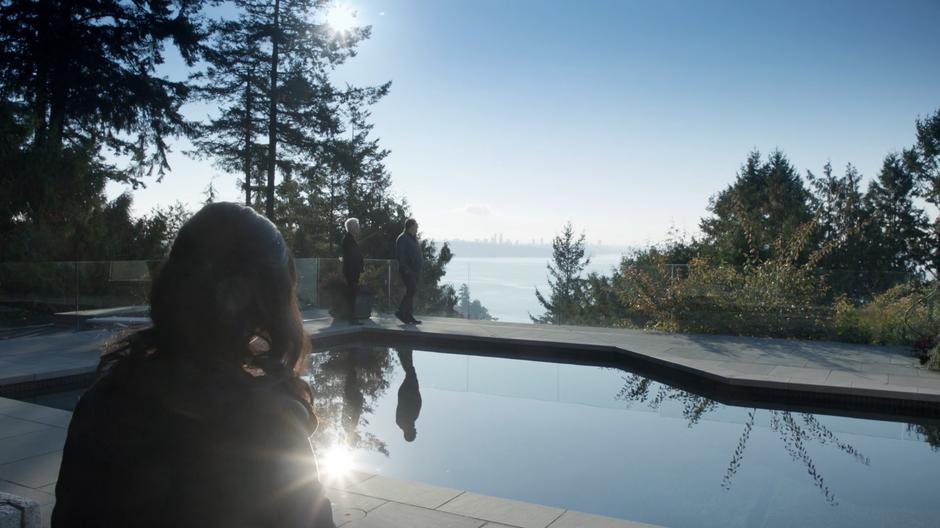 Blaine walks with a potential buyer of the brain on the far side of the pool looking out over the skyline while Darcy Bennett sits and waits.