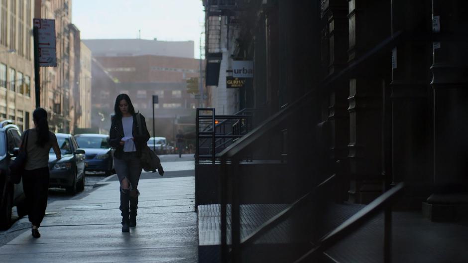 Jessica looks down at the list of addresses while walking down the sidewalk.