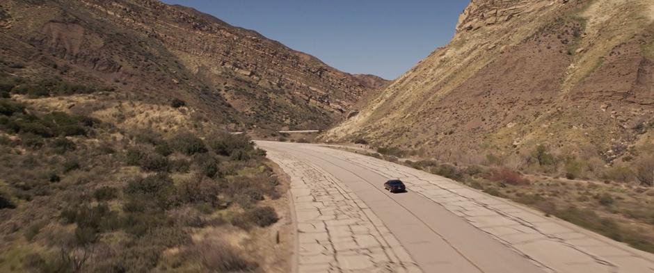 Fury and Vers drive down an empty and rundown road in the remote mountains.