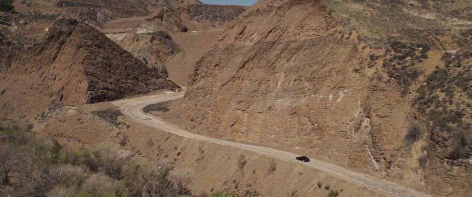 Fury drives his car down the road past several large hills.