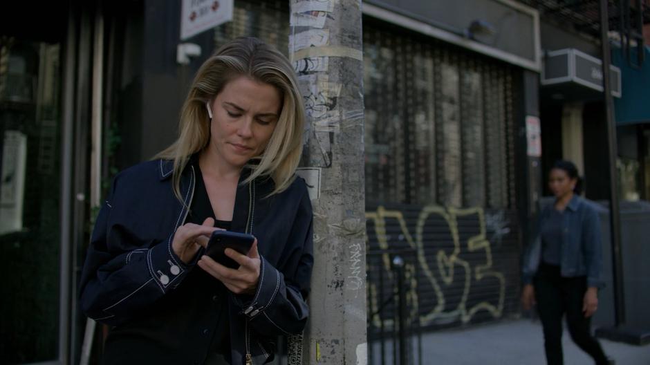 Trish leans against a light pole while checking her phone.