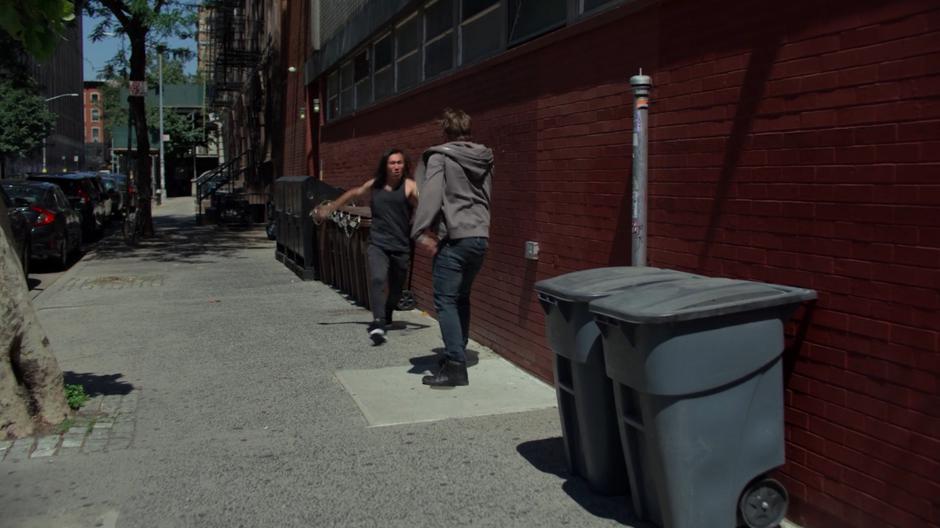 Two dudes playfully fight on the sidewalk.