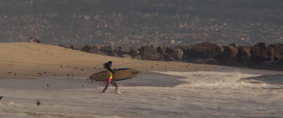 A woman walks into the water with her surfboard.