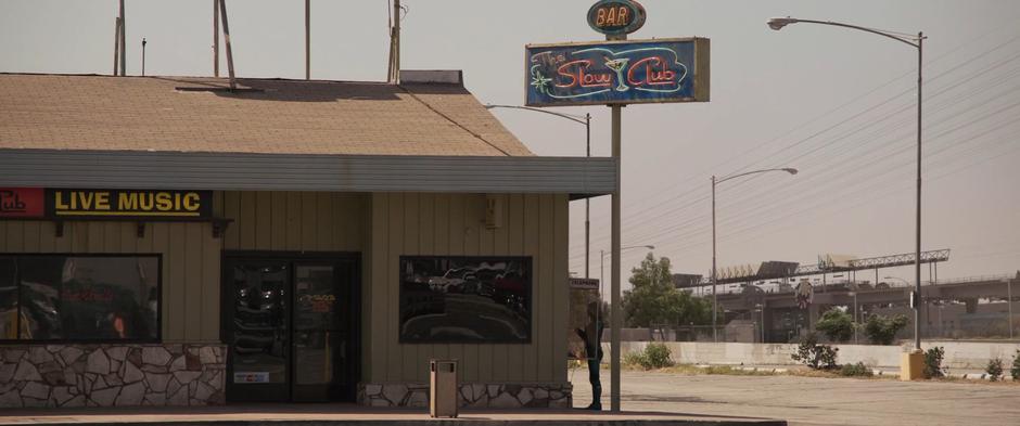 Vers stands at a payphone next to the bar making a call.