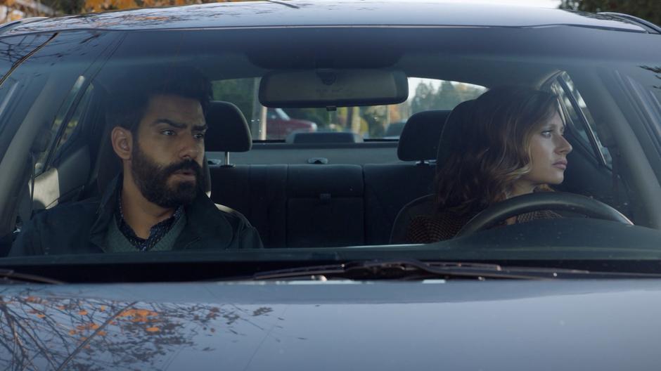 Ravi and Peyton sit in the car on the street outside the house.